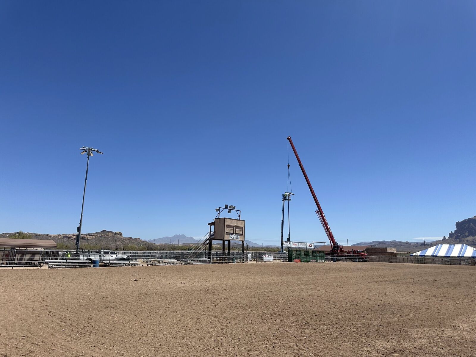 Crane setting a lighting pole at a desert rodeo arena under open sky